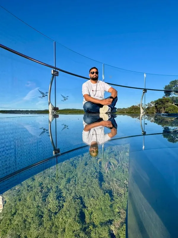 Huiatã Ribeiro sentado num mirante de vidro, com o céu refletido no piso